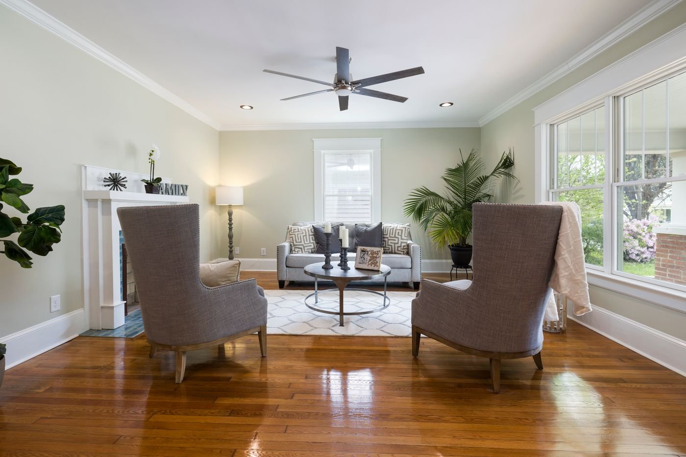 Salon chaleureux avec fauteuils, canapé et parquet brillant reflétant la lumière naturelle